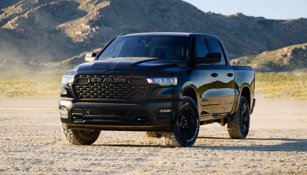 Front three-quarter view of a black RAM 1500 truck on sandy terrain outdoors.
