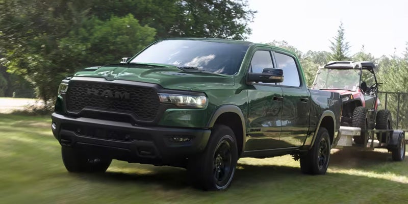 Green RAM pickup truck towing an off-road vehicle on a trailer.